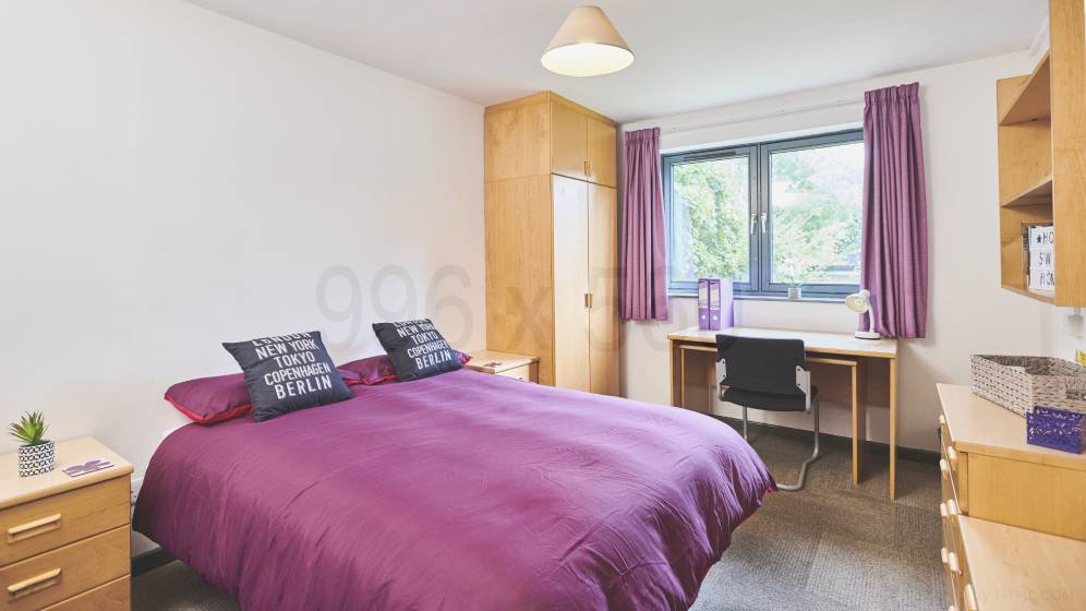 The master bedroom within the family and couple flats. There is a double bed, two bedside tables, a desk and chair, two sets of drawers, a wardrobe and some shelving.